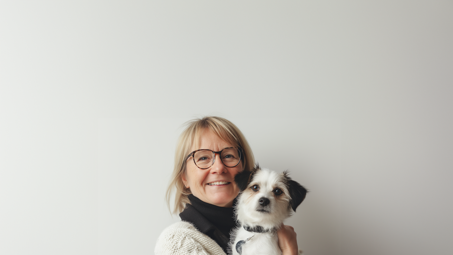 A smiling owner holding her small black and white dog during a consultation
